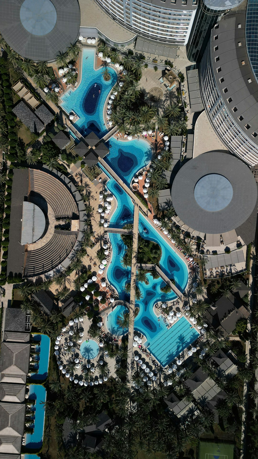 Aerial view of a luxurious swimming pool complex featuring multiple interconnected pools, surrounded by palm trees and lounge chairs, highlighting the inviting atmosphere of a resort-style setting.