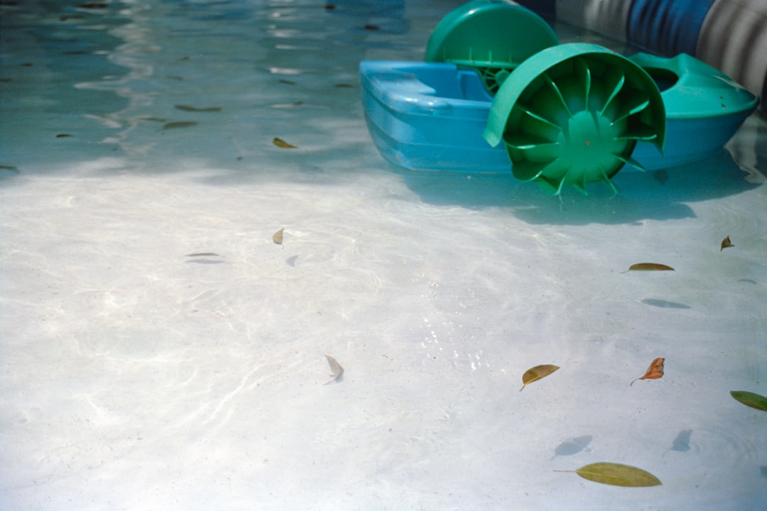 Pool water with a turquoise cleaning device and scattered leaves, illustrating the importance of regular maintenance for clear water in pool cleaning services.
