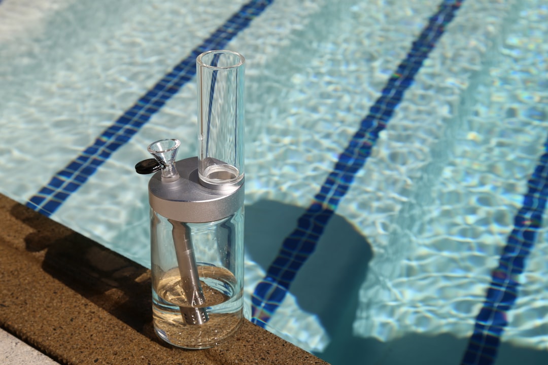 Bong placed on the edge of a pool, with clear water and blue tile lines visible in the background, emphasizing pool inspection services.